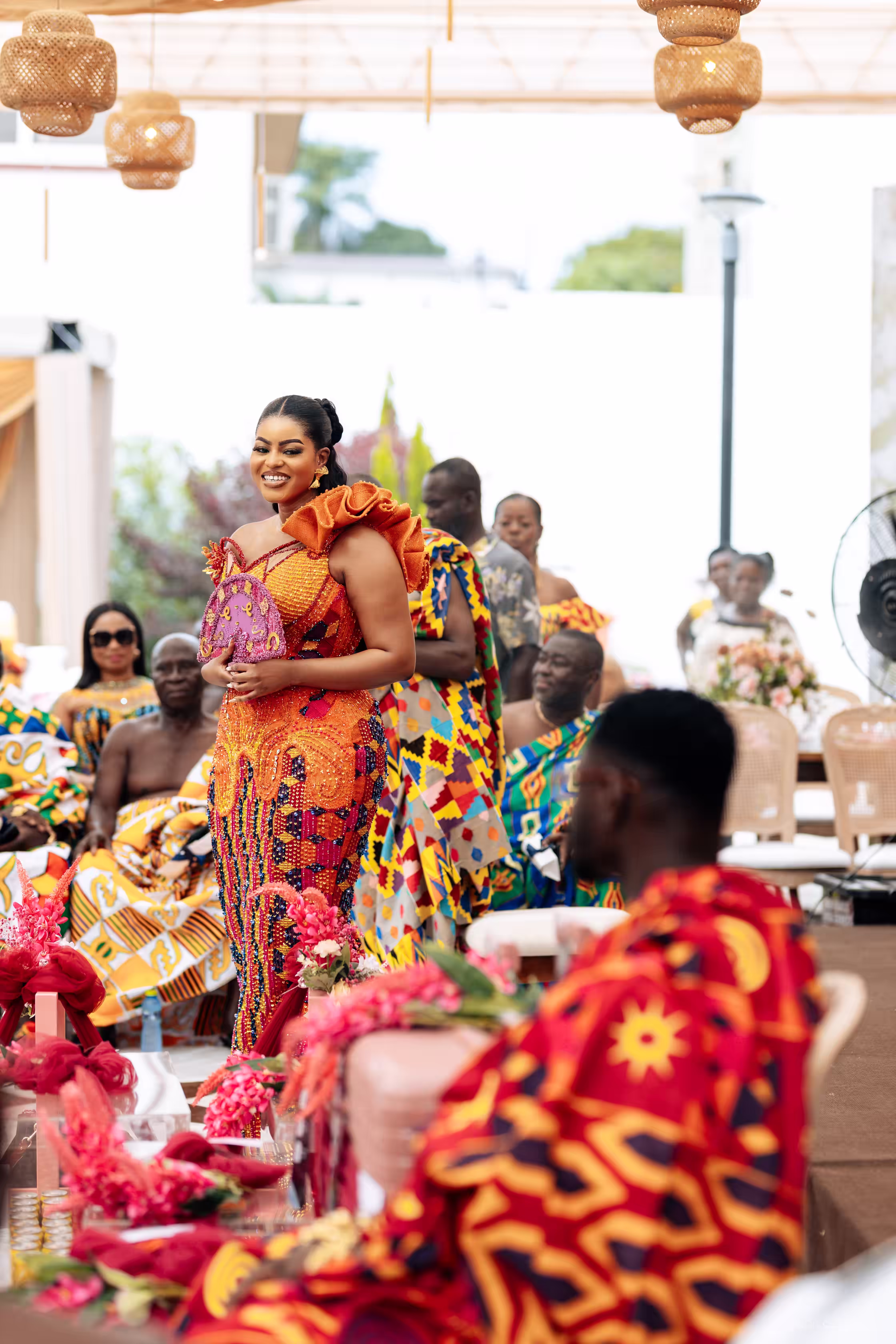 Cassie arriving at the ceremony in a beaded kente gown as family looks on in traditional cloth