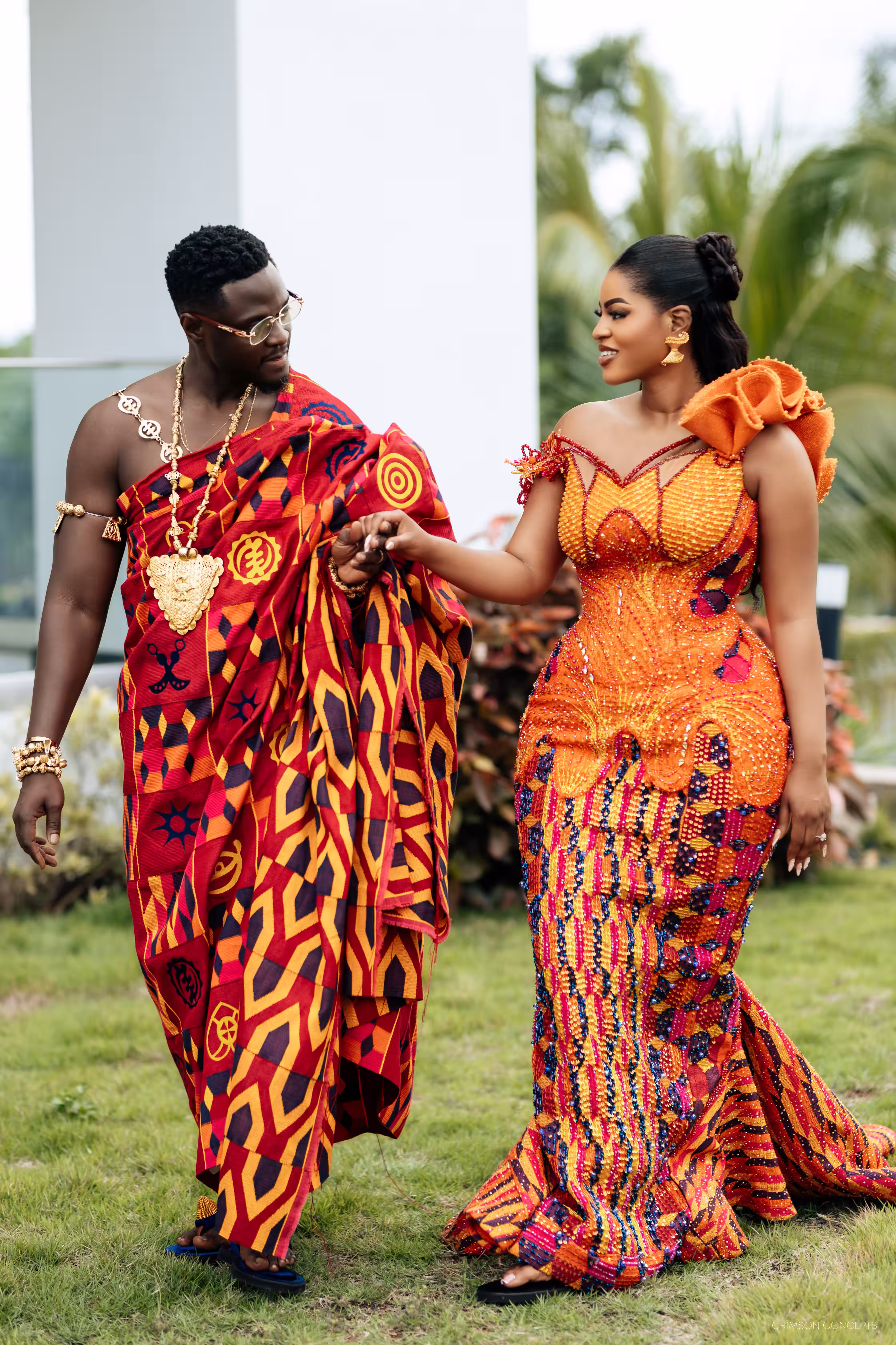 Qojoh and Cassie walking hand in hand in traditional kente after their Kumasi wedding ceremony