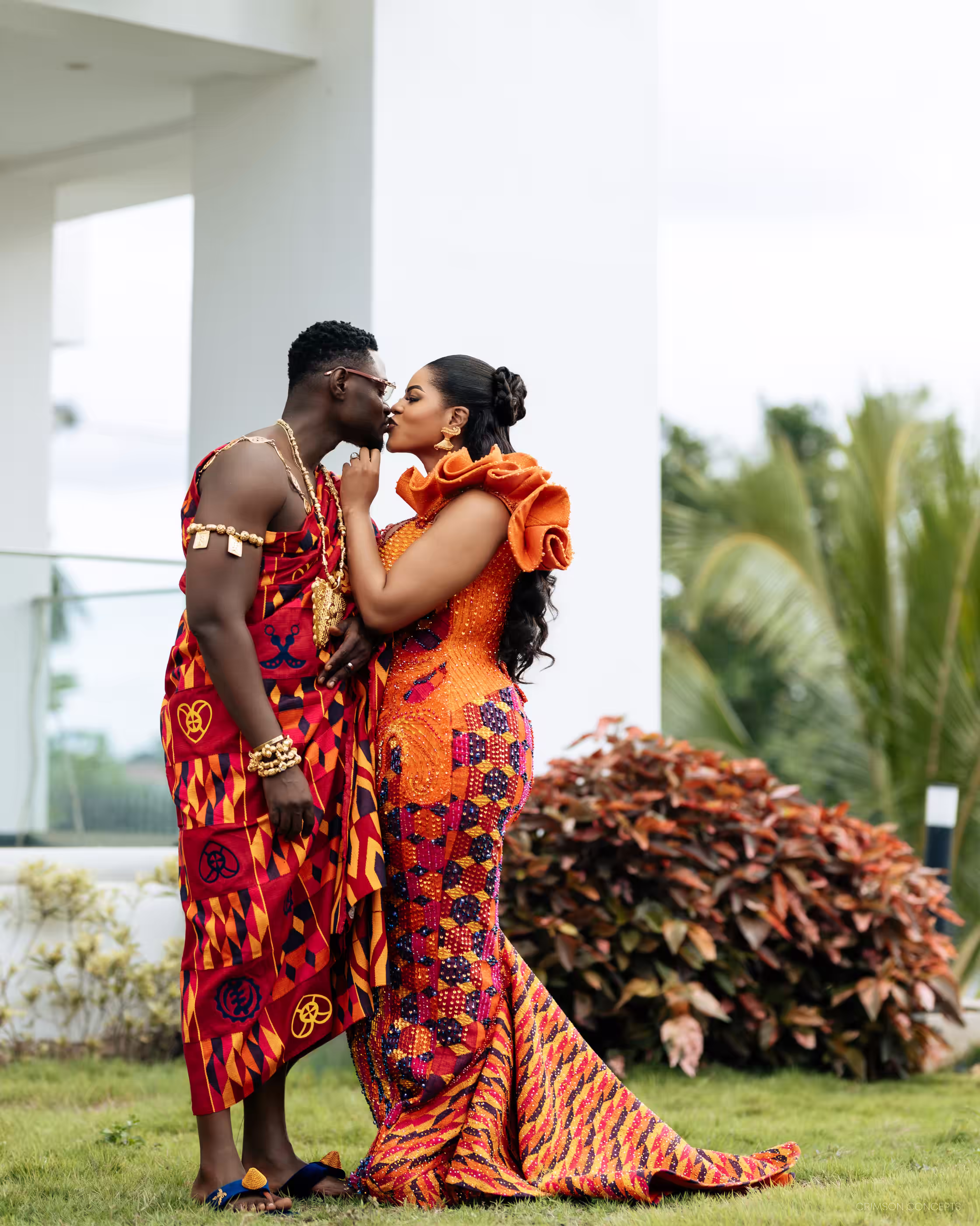 Qojoh and Cassie share a kiss in the garden, both dressed in kente for their traditional wedding